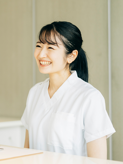⽩い制服を着⽤し、受付カウンターで笑顔を⾒せる医療事務スタッフのイメージ