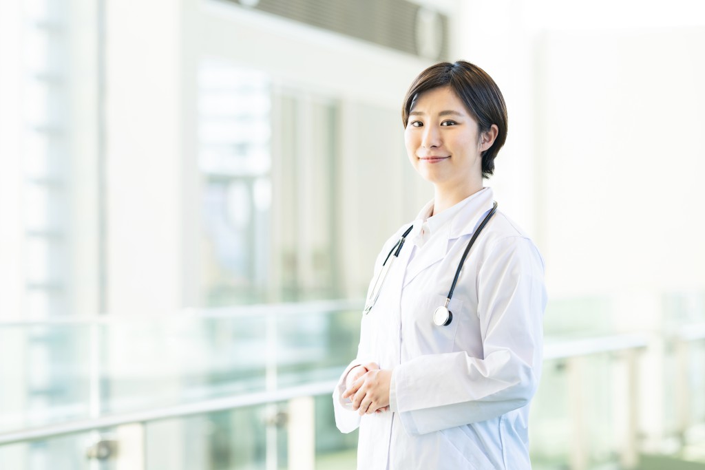⾸に聴診器をかけ、前を向いて微笑む⼥性医師のイメージ