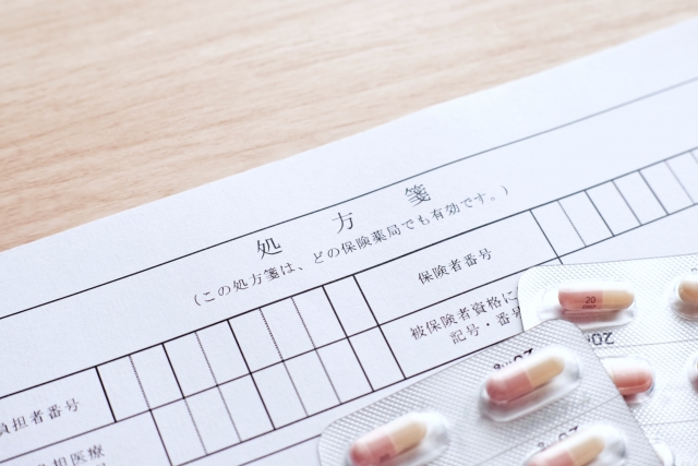 木目のテーブルの上に置かれた処方箋の用紙とカプセル薬のシート